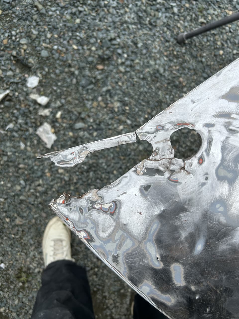 Close view of the bottom of a stripped fender, the end torn and pitted through by rust