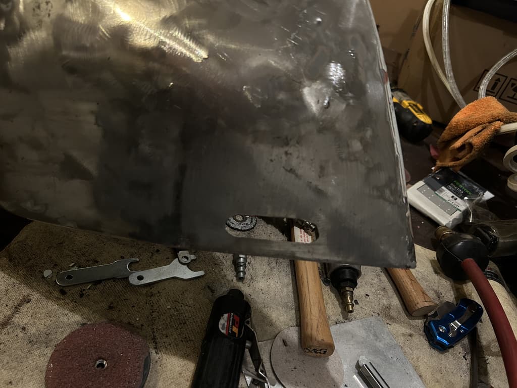 A bare-metal body panel on the workbench surrounded by grinders, hammers and cutting discs