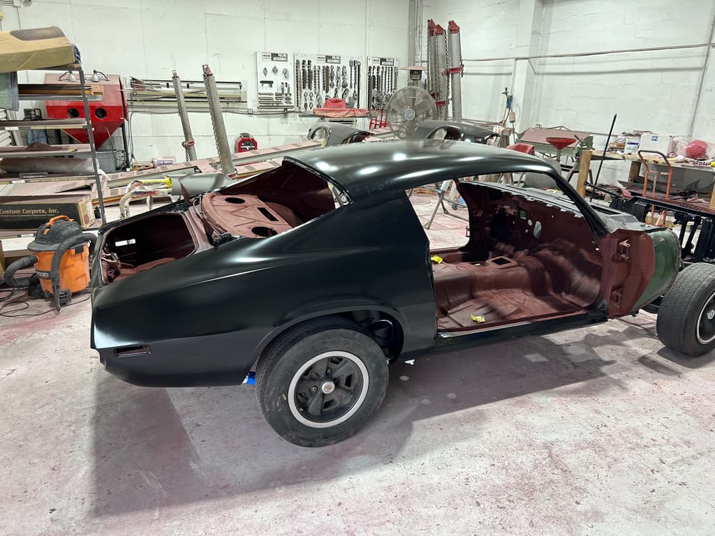 Side view of the Camaro body in glossy black epoxy primer, interior in red oxide
