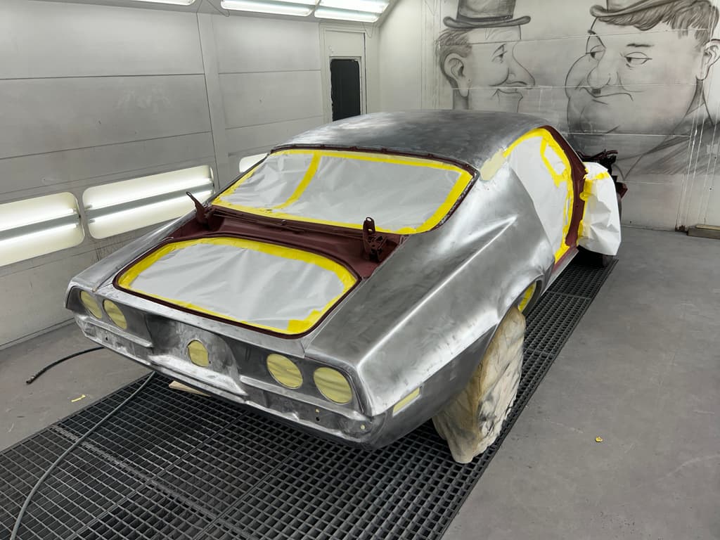 Bare-metal Camaro body in the spray booth with the window openings and trunk masked with paper and yellow tape
