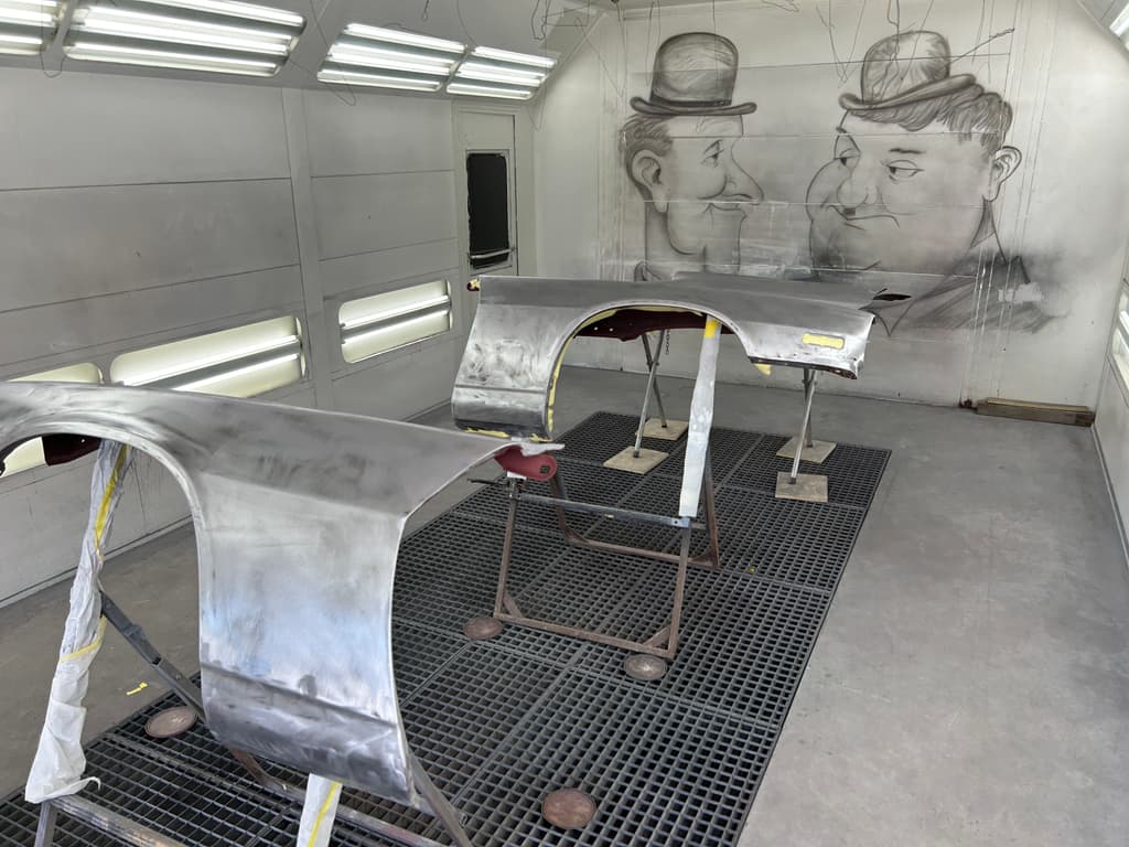 Two bare-metal fenders on stands in the spray booth, edges masked, ready for primer