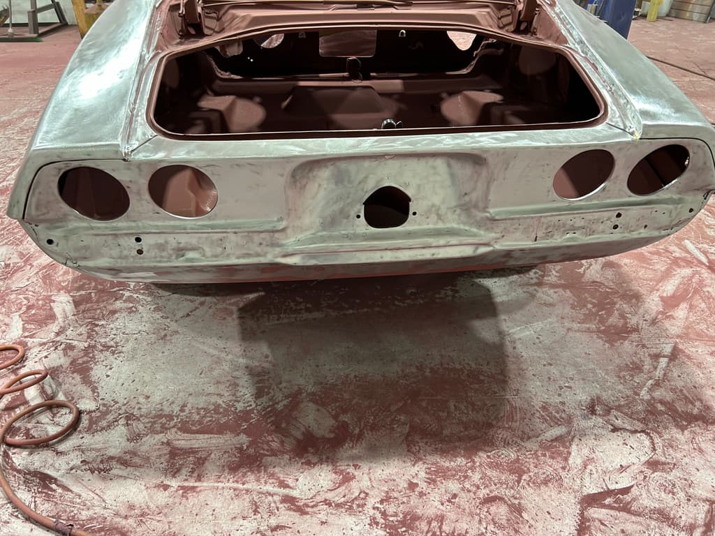 Rear panel of the Camaro in bare metal, with four round tail light openings and the empty trunk in red oxide primer