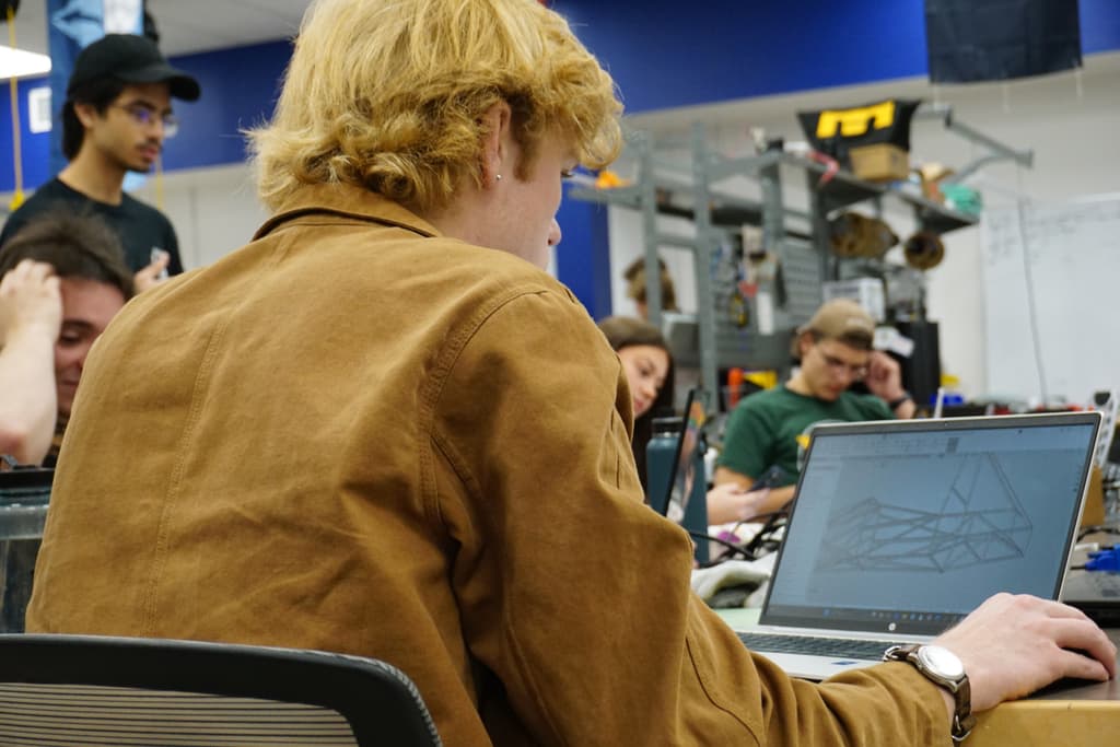 Patrick at a laptop showing the Formula MUN chassis space frame model, with team members working around him