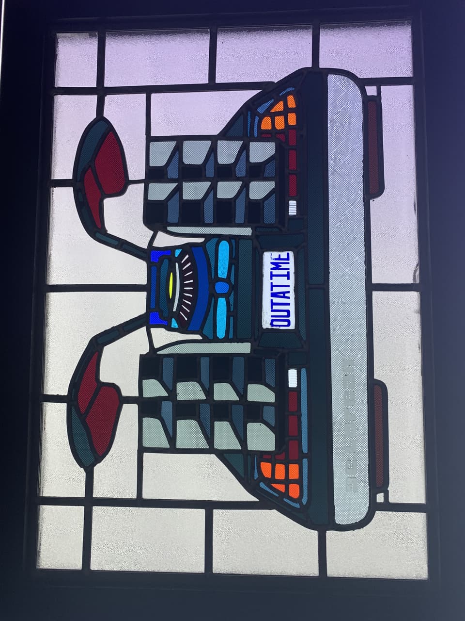 Finished stained glass panel of the rear of the DeLorean from Back to the Future, lit from behind in a window