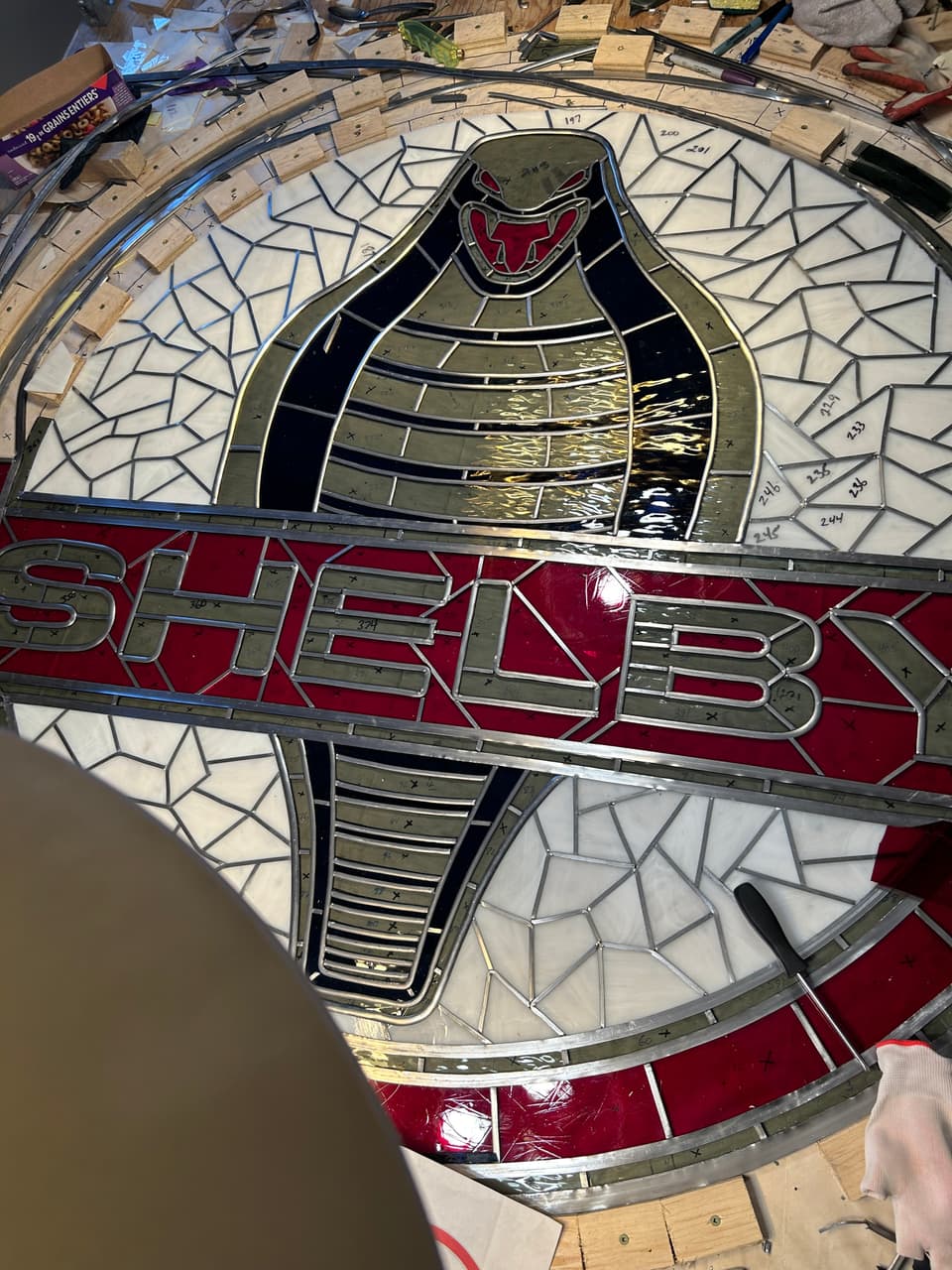 Close view of the Shelby lettering and snake, showing grey lead came lines and soldered joints between red, white and dark glass