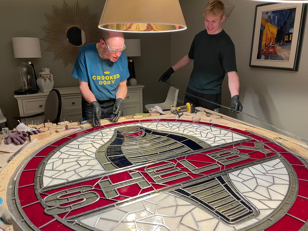 Patrick and his father in gloves working on the 5 ft circular Shelby panel laid flat on a large table