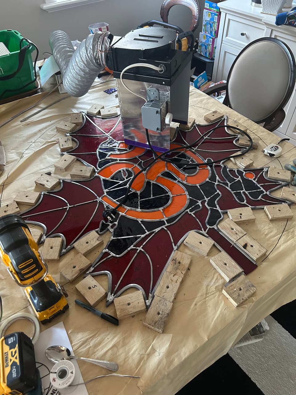 Glass grinder on the table beside the partly built temple panel, with the orange Om symbol and red maple leaf pieces held in place by wooden strips