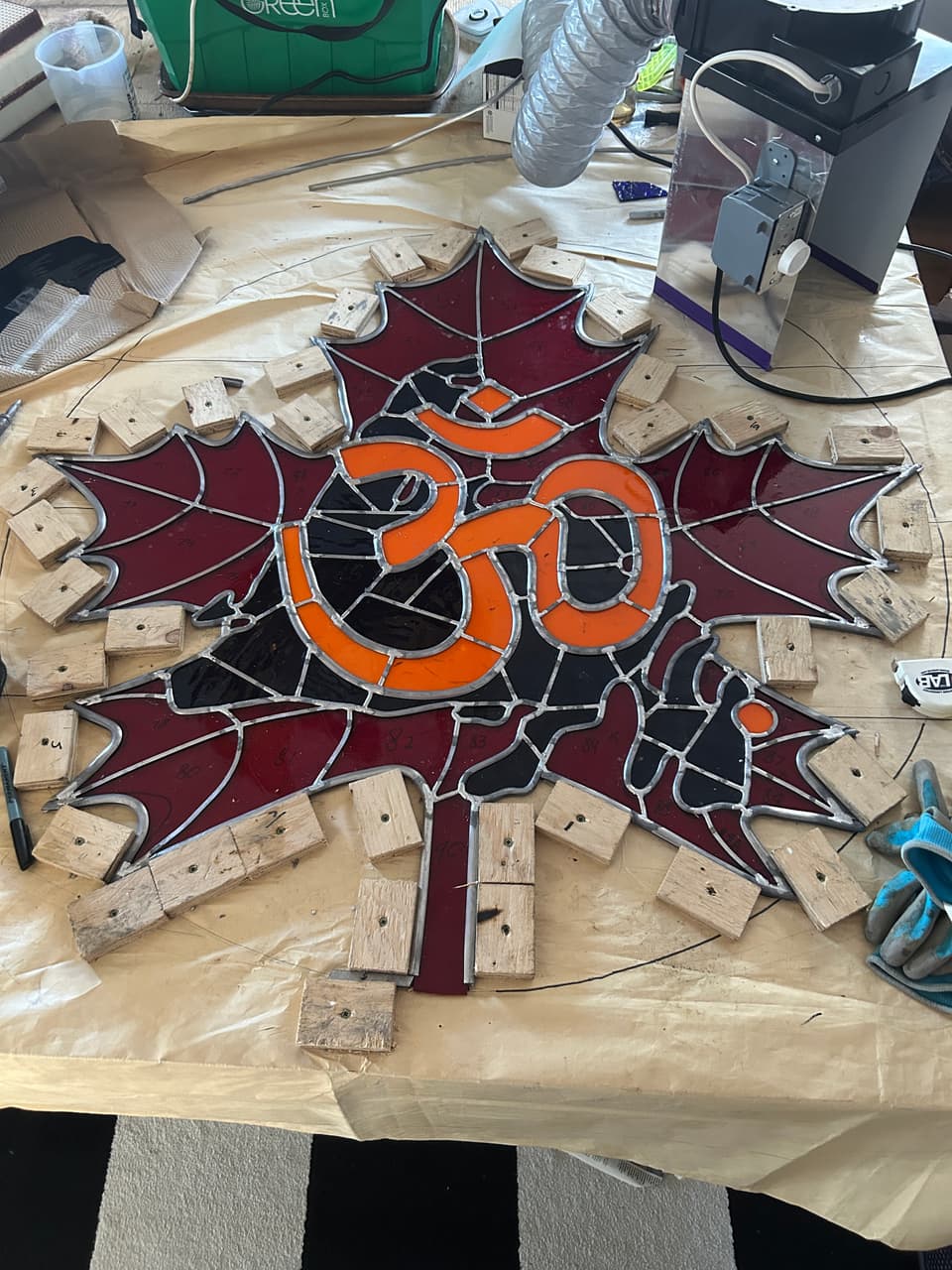 The red maple leaf and orange Om symbol assembled in lead came, held by wooden strips on the work table