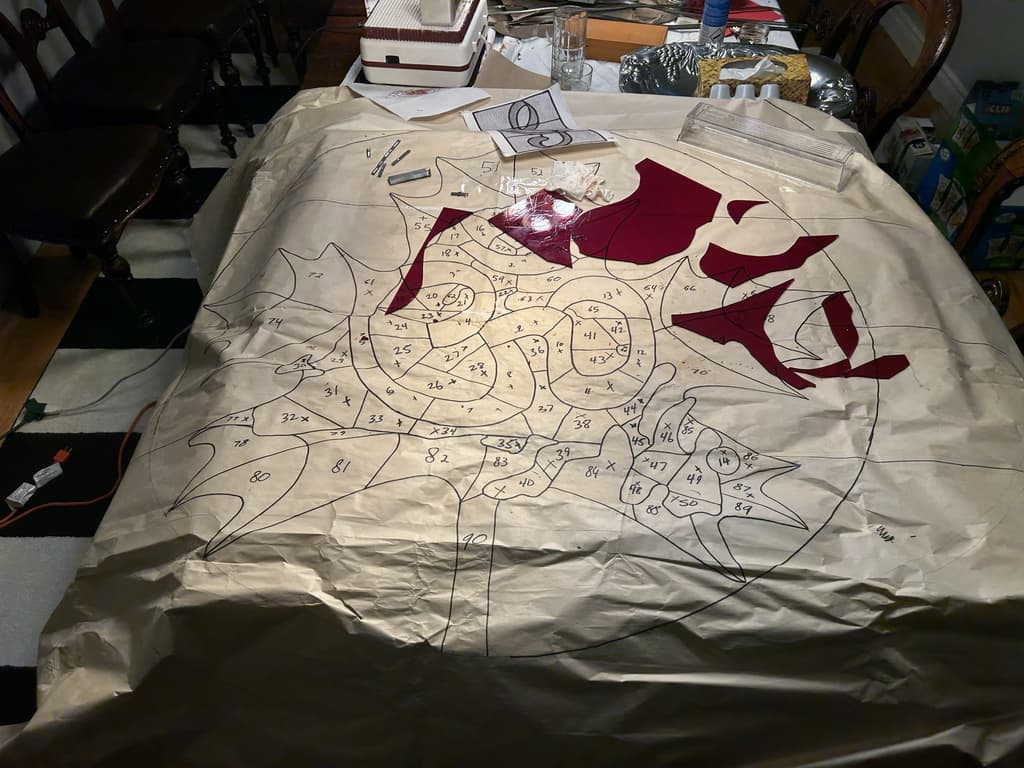 Full-size paper pattern for the temple panel covering a table, every piece outlined and numbered, with the first red glass pieces placed on it